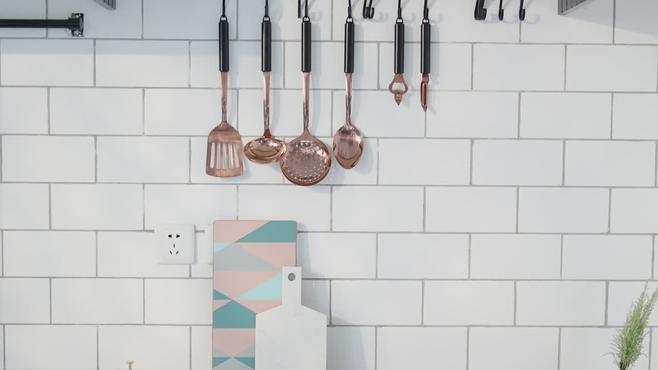 A bright, minimal kitchen wall features copper utensils, geometric cutting boards, cookbooks, herbs, and fresh produce arranged with clean aesthetics.