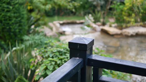una valla de madera negra con vistas a un estanque tranquilo en un jardín verde exuberante