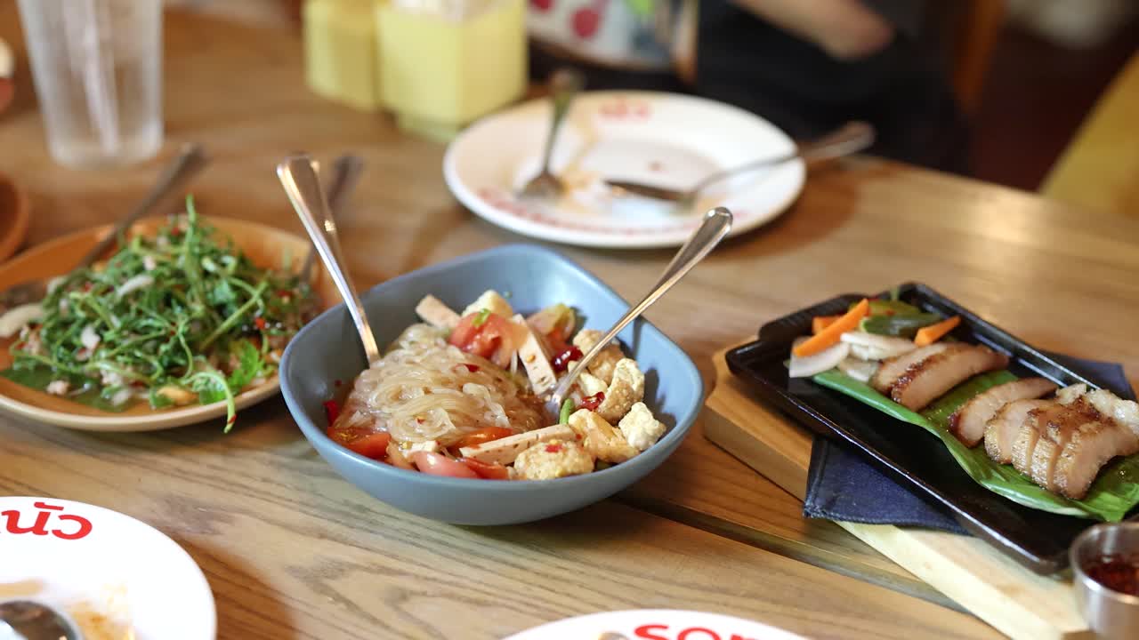 Assorted Thai cuisine on wooden table, natural lighting, slight camera pan, casual dining atmosphere