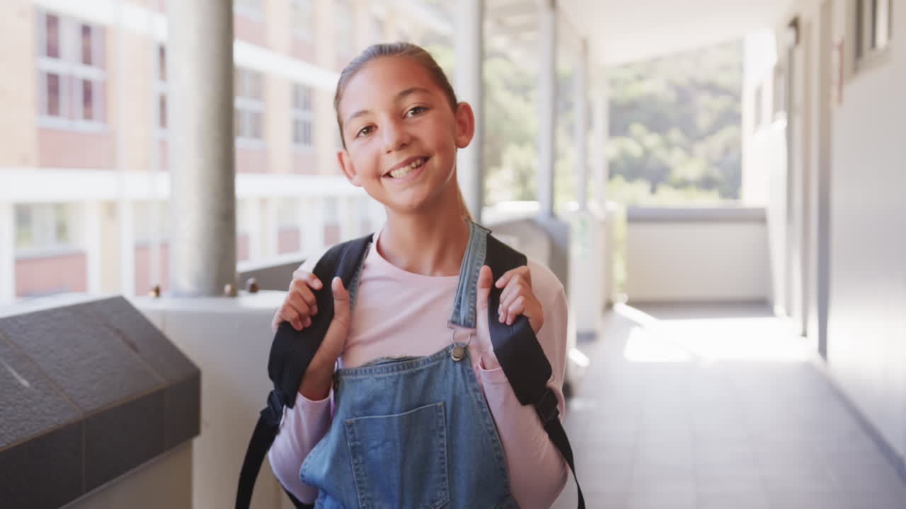 Smiling girl with backpack standing in school hallway, ready for class