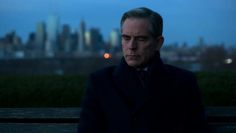 man sitting on a park bench with a city skyline at dusk
