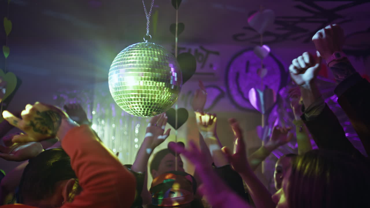 Crowd moving dance floor under vivid disco ball glow. Happy young people dancing
