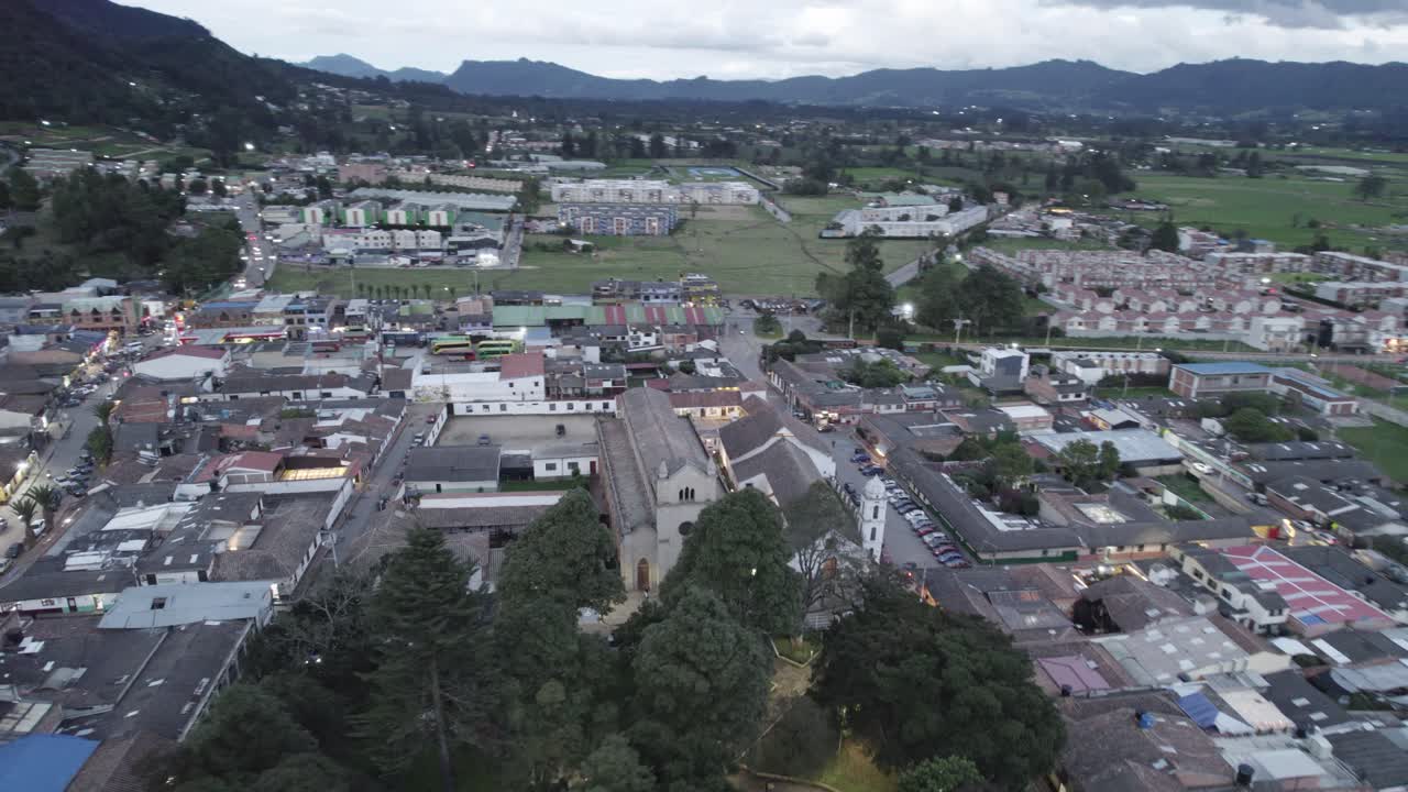 Ascending semi orbit aerial of Tenjo town, Colombia, highlighting colonial church and central square at dusk