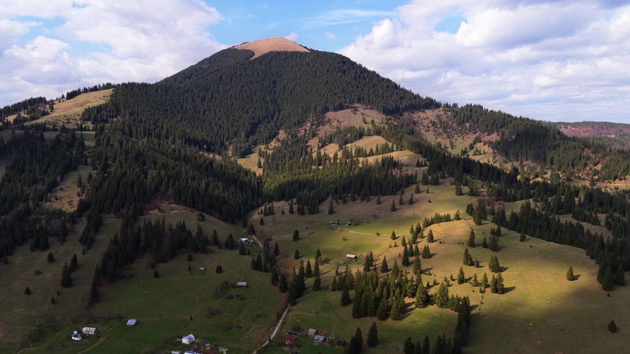 Veduta aerea con drone su dolci colline coperte da foreste e radure aperte, con una singola cima montuosa che si erge sullo sfondo, Passo Mestecanis, Romania