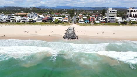 Gente-En-La-Arena-Con-Espigón-De-Roca---Verano-En-Palm-Beach,-Gold-Coast,-Qld---Tiro-De-Dron-De-Retroceso