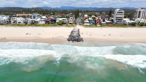 gente en la arena con espigón de roca - verano en palm beach, gold coast, qld - tiro de dron de retroceso