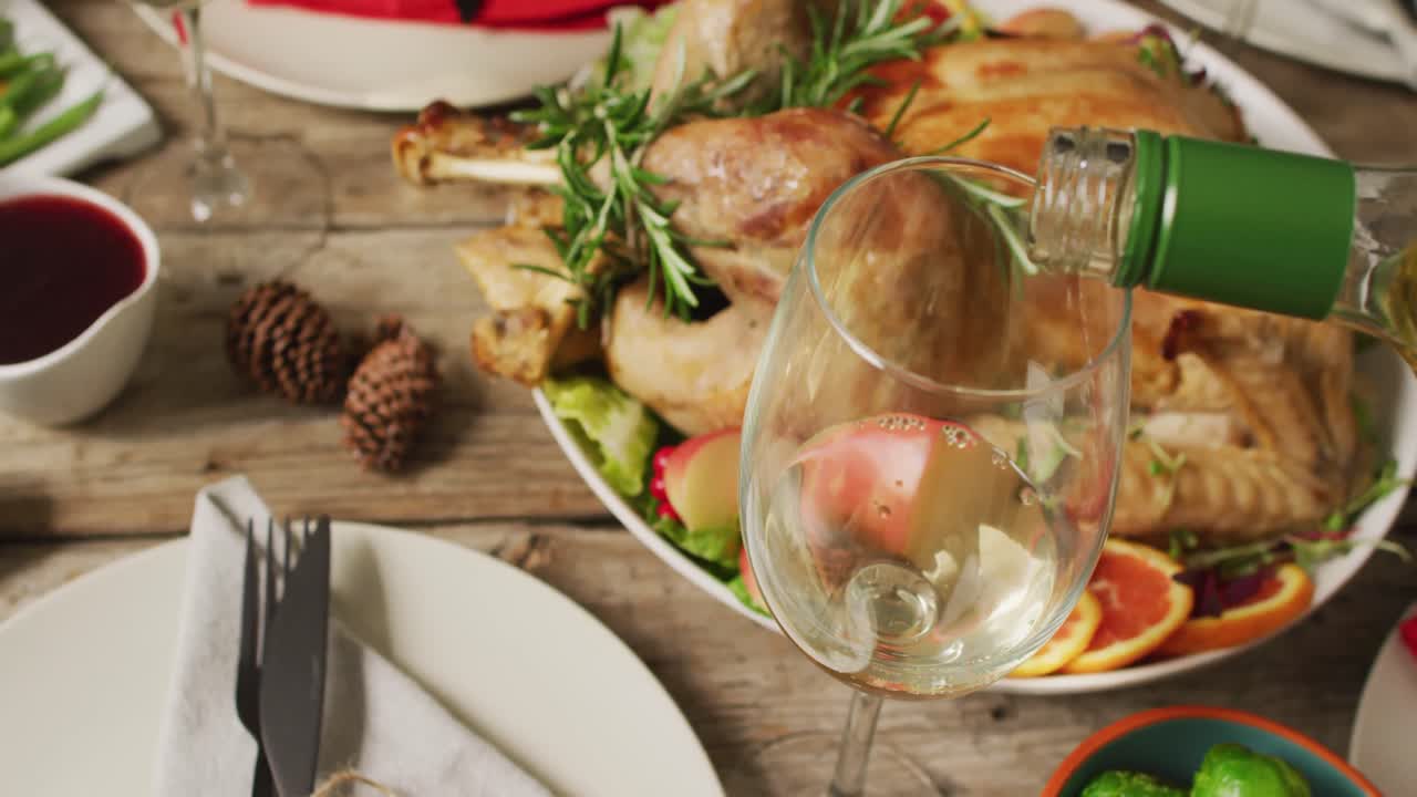 video de bandeja con pavo asado, platos diversos y vino vertiendo en vaso en superficie de madera