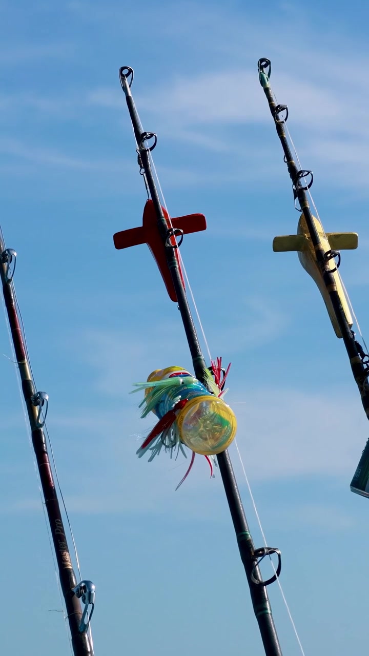 Fishing rods with colorful lures sway gently against a clear blue sky in Phuket, Thailand. Bright daylight enhances the vivid colors
