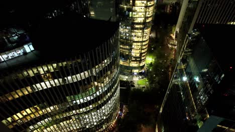 aerial drone night of santiago de chile business offices at nueva las condes neighborhood, fly around lightened architecture with windows towards city streets