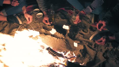 view from the top: young people holding sticks with marshmallows and frying them at night. group of people sitting by the fire late at night