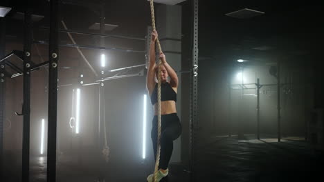 sporty exercise for endurance and power woman is climbing rope in fitness hall