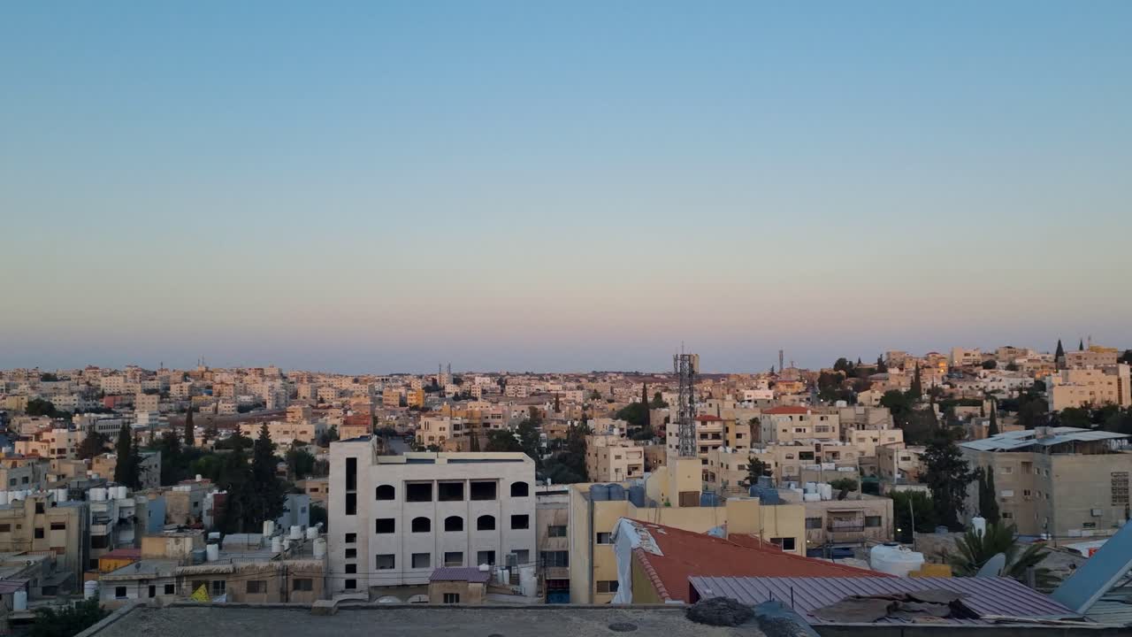 Panoramic skyline view over Madaba, Jordan, with evening sun illuminating rooftops and the city stretching across rolling hills toward the distant horizon