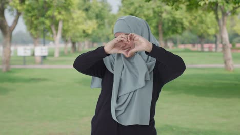 happy muslim woman showing heart sign in park