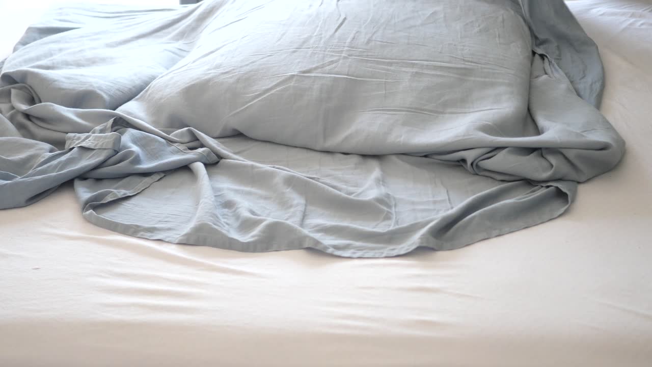 cama sin hacer con ropa de cama gris