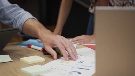 Mid-section-of-diverse-male-and-female-colleagues-in-discussion-using-notes-in-office,-slow-motion