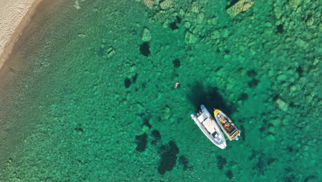 girl swimming next to speed boats in the aegean sea off the greek island of ios