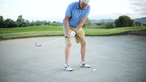 cinematic slow motion shot of a golfer hitting the golf ball out of the sand trap and onto the green