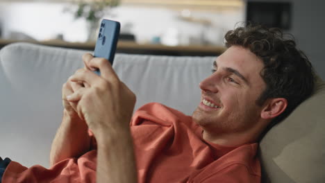 Happy guy laying couch messaging mobile phone closeup. Carefree man chilling
