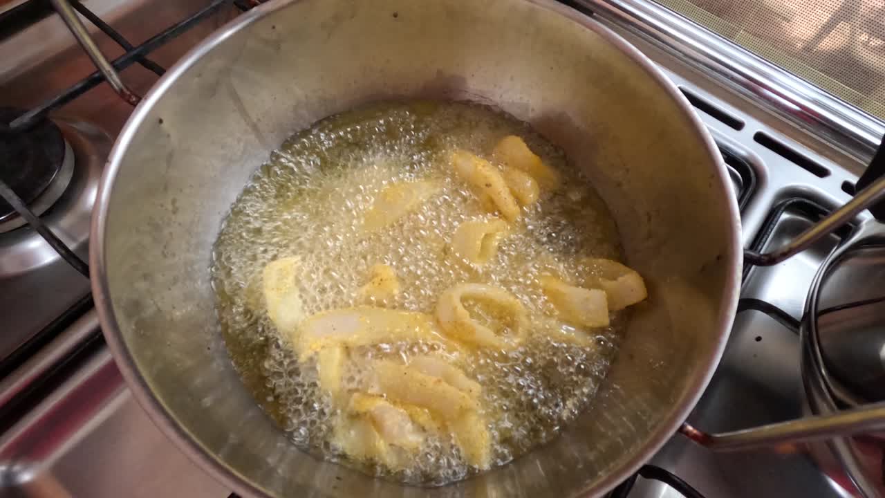 Anelli di calamari marocchini croccanti vengono fritti in olio bollente e ricoperti di pastella aromatizzata durante la preparazione tradizionale di frutti di mare. Una schiumarola solleva gli anelli appena cotti dall'olio caldo mentre ad