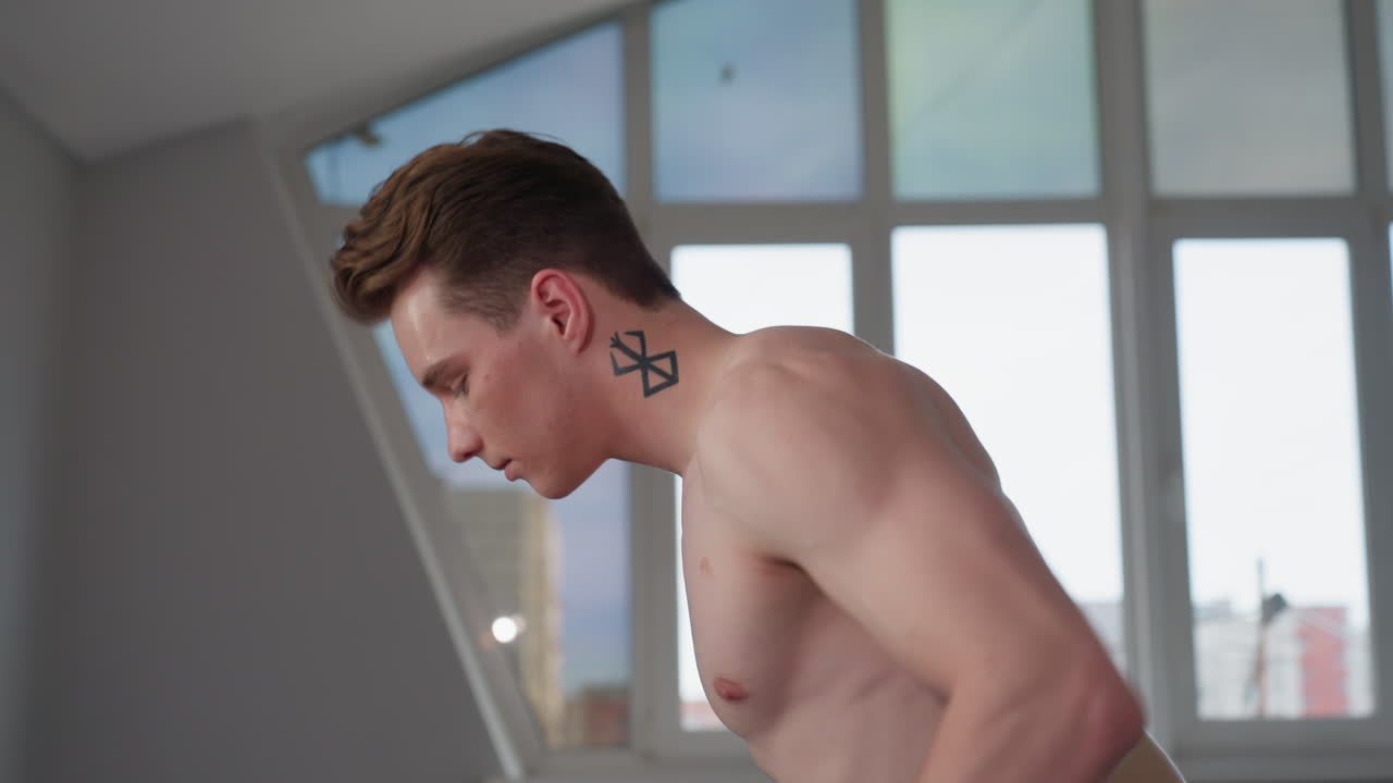 close up of focused high school boy with geometric neck tattoo during workout in naturally lit room, sweat visible on forehead, posture leaning forward with intensity and determination
