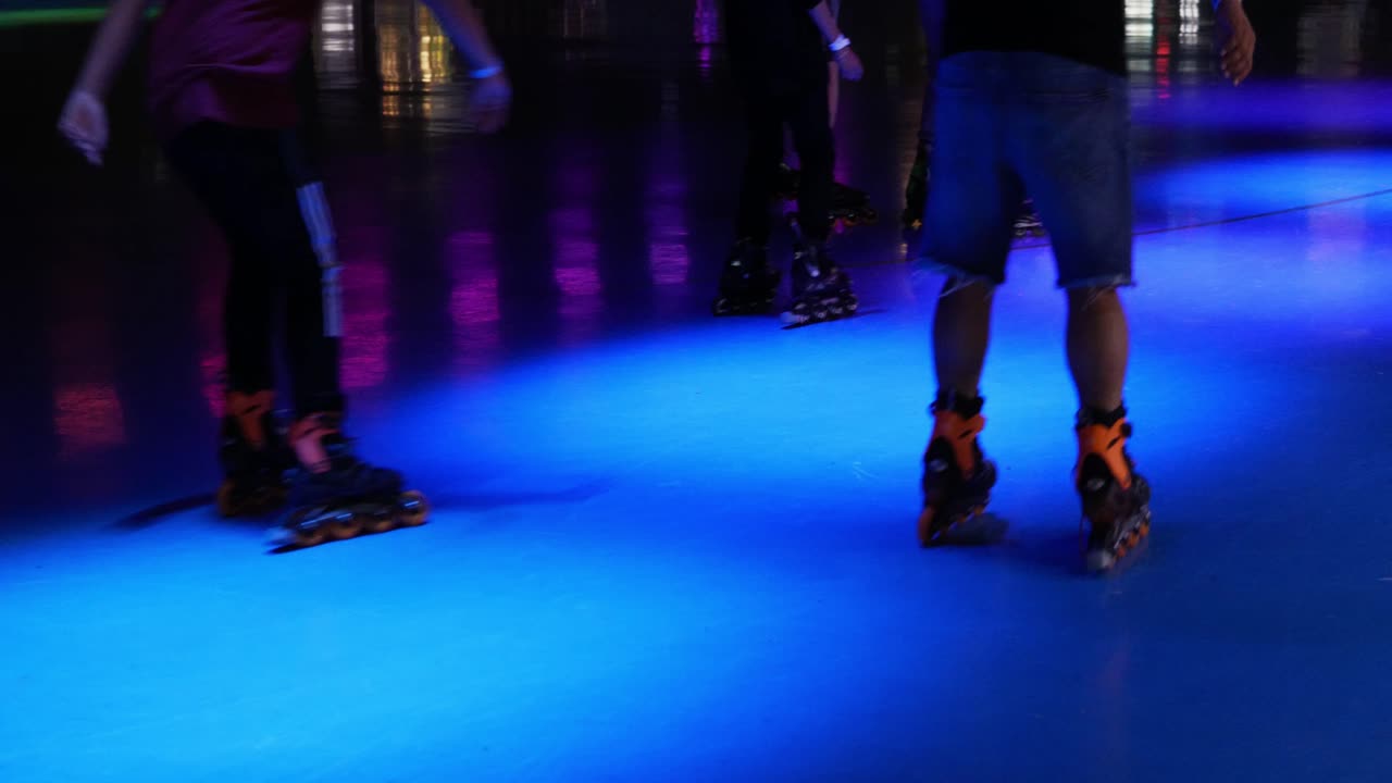 Busy roller skating rink with rollerblades and rollerskates on people as they skate around brightly colored party scene venue - in Cinema 4k (30fps slowed from 60fps).