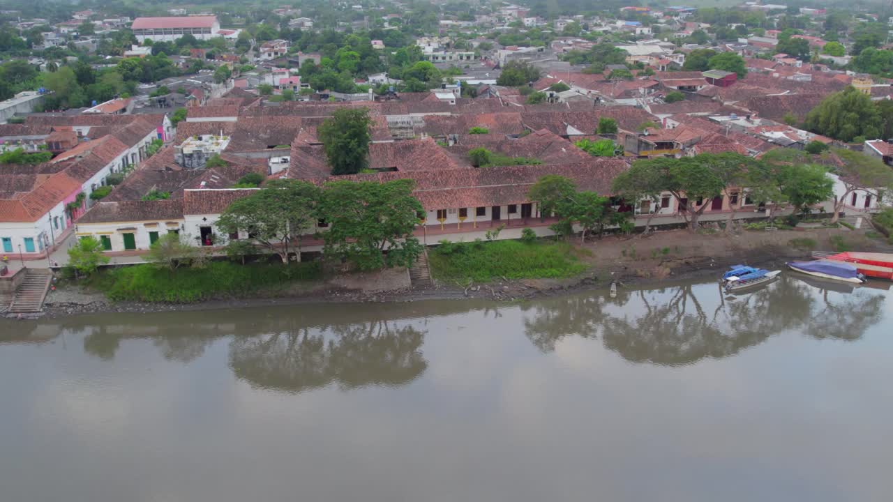As the drone moves, the riverside buildings come into view, their colonial facades standing in quiet harmony with the natural landscape. Roll right.