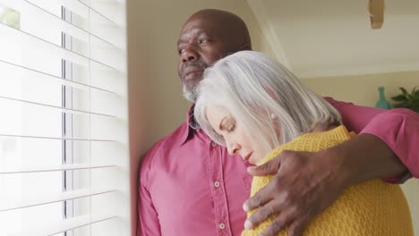 Senior-diverse-couple-embracing-and-looking-through-window