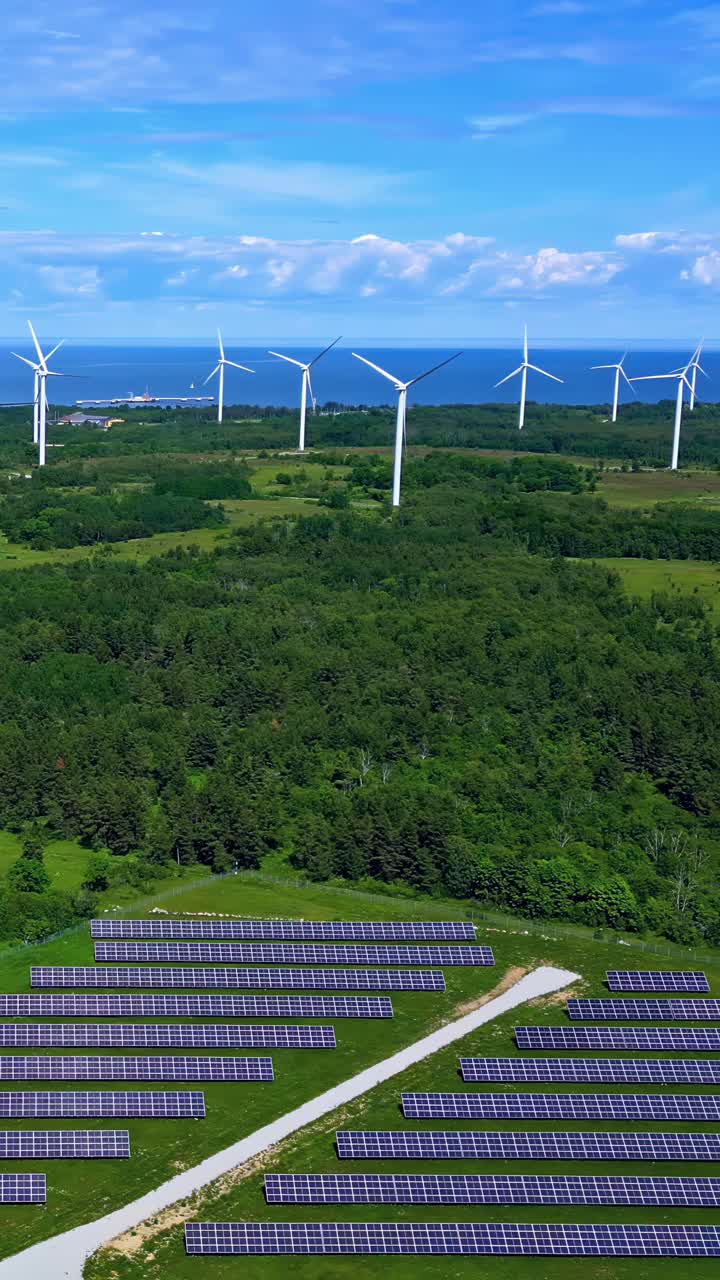 Paneles solares y turbinas en la costa generando energía limpia en una granja sostenible amplia, toma aérea vertical de establecimiento