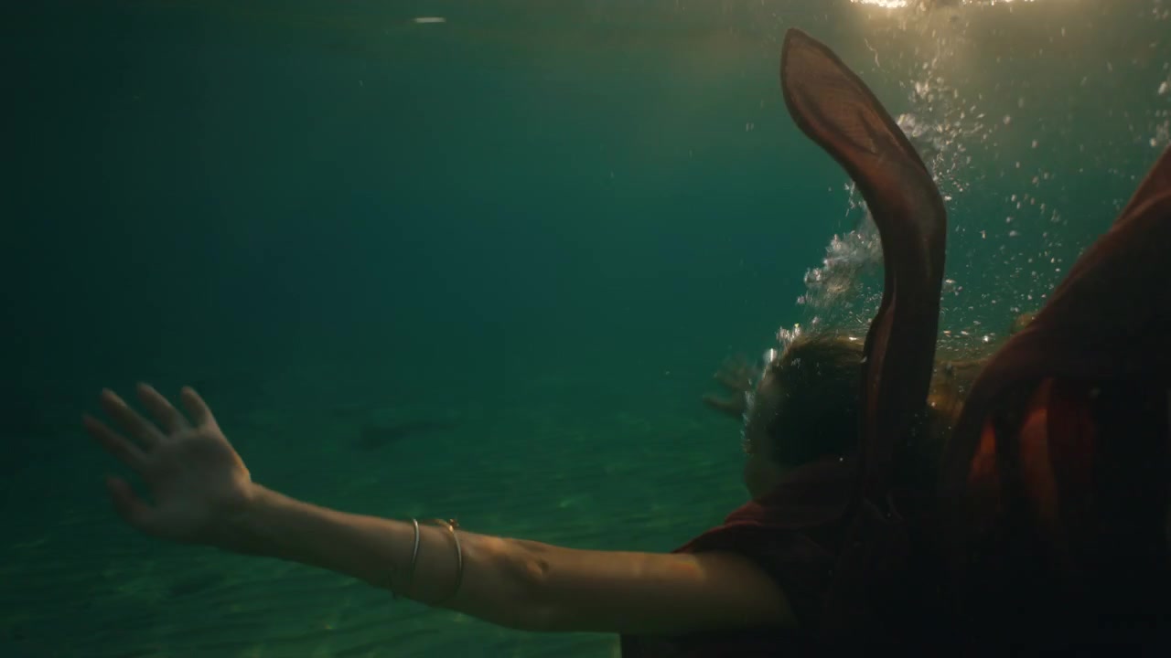 Pies que se adentran en el mar mientras un vestido vaporoso se mece con la luz de la hora dorada.