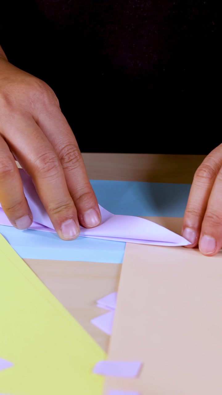 Person’s hands carefully fold colored origami paper on table, under bright, even lighting, close-up