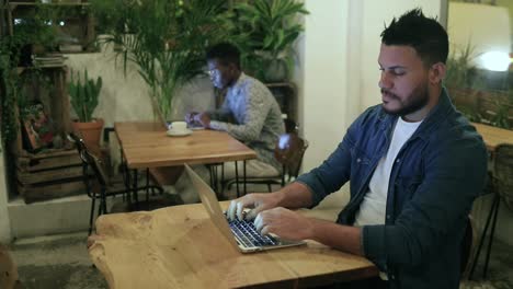 hombres jóvenes multirraciales que usan computadoras portátiles en una cafetería