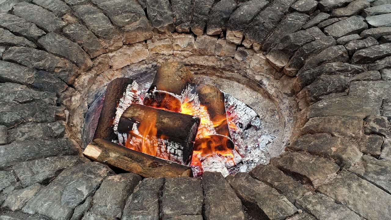 hermoso pozo de fuego de piedra circular con llamas, brasas y troncos ardientes durante un frío día de invierno al aire libre en el jardín