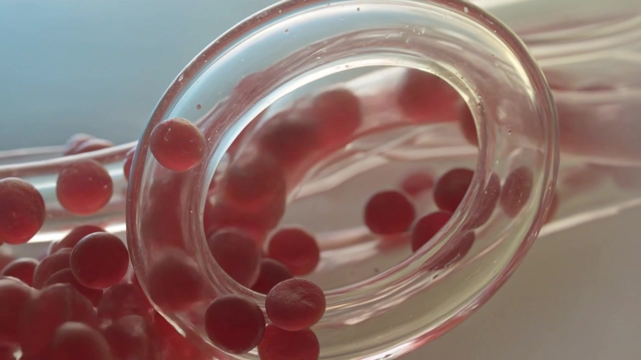 Approaching from left, pink beads entering clear looped tube in close-up, moving right to continue