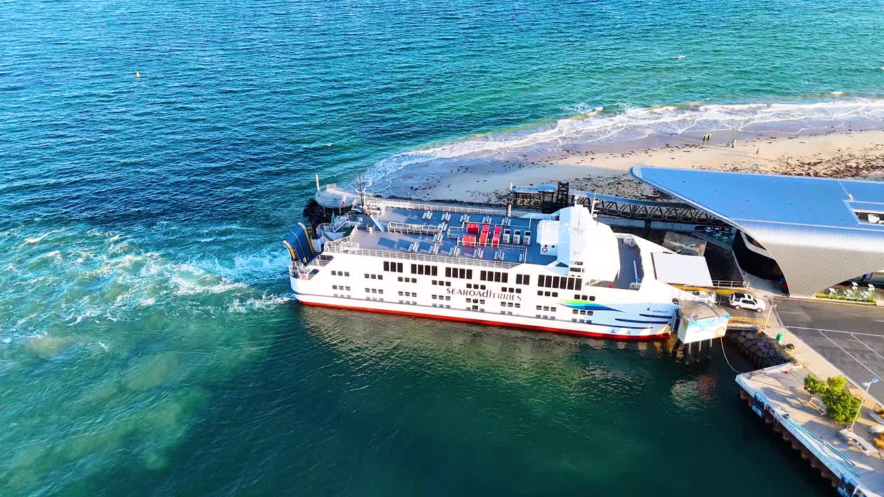 Aerial view of a ferry docking at Queenscliff terminal in clear daylight, showcasing smooth maneuvering and vibrant coastal scenery