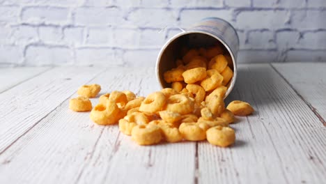 cheese puffs spilling out of container on a white wooden table