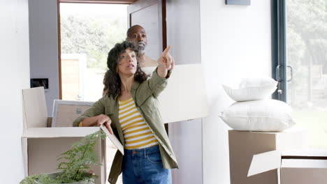 una feliz pareja biracial hablando y llevando cartones en la nueva casa, en cámara lenta