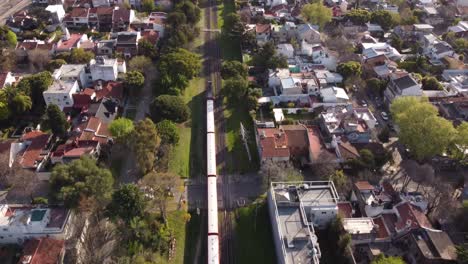 aerial view of red train passing by residential housing in buenos aires, argentina