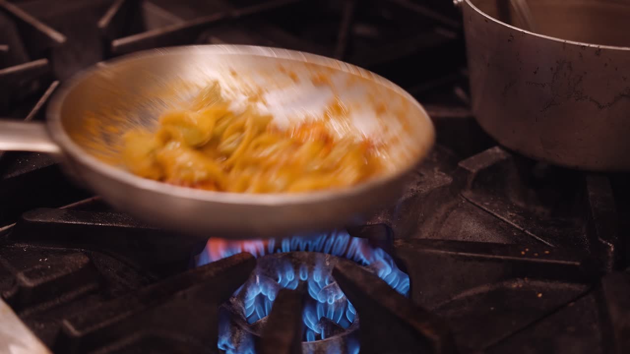 la pasta se agita en una sartén plateada en la estufa de gas en la cocina de un restaurante
