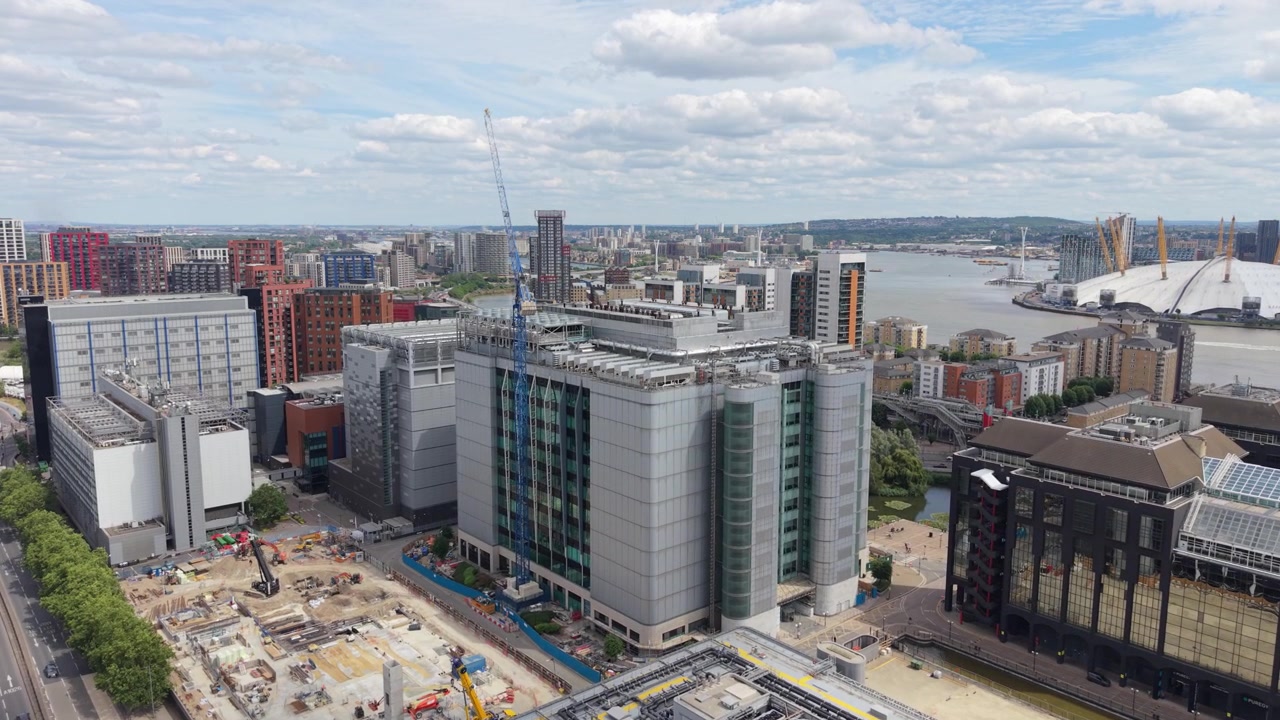 High-angle shot shows a large Data Center building under a blue sky in London. Nearby construction is visible. The O2 Arena and River Thames are in the background, with other city architecture.