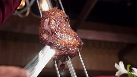 gaucho slices juicy beef from skewer at brazilian steakhouse, slow motion 4k