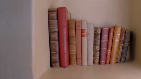Slow-dolly-shot-of-a-small-collection-of-antique-books-on-a-shelf