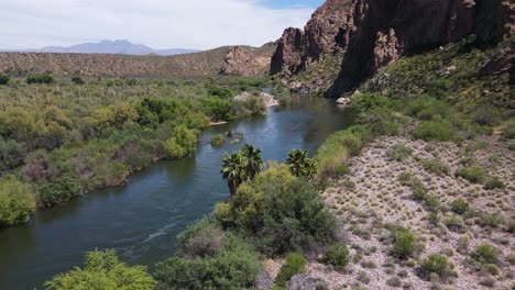 Scenic-view-of-River-Flowing-in-Desert-with-Palm-Trees-in-Foreground,-Mountains-in-Background,-Salt-River-and-Four-Peaks-Mountain