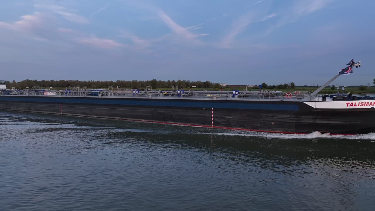 A large cargo ship cruises along a peaceful river during a serene sunset