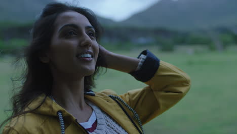 independent young indian woman looking up running hand through hair smiling happy enjoying gentle breeze on travel adventure alone in peaceful countryside
