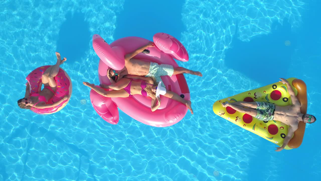 DRONE Young tourists smile while chilling out at the pool during summer vacation