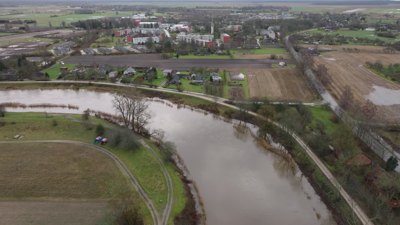 Aerial establishing view of high water in springtime, Barta river flood, brown and muddy water, overcast day, wide drone shot moving forward, tilt down