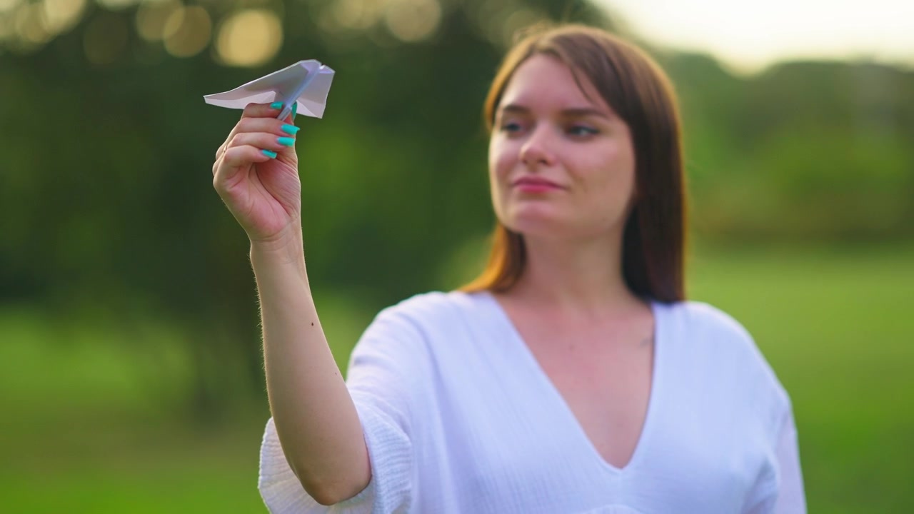 Giovane donna che tiene un aeroplano di carta in un parco verde.