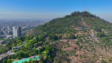 reveal drone shot of san cristóbal hill in santiago, featuring cable cars, greenery, and distant city views