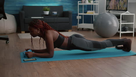 flexible slim black woman stretching body muscles putting cronometer on phone