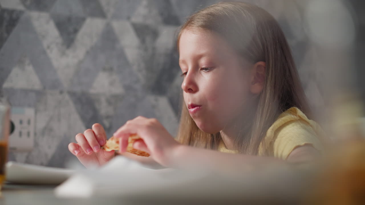 close up of cute child in yellow shirt eating grilled egg cheesy pizza at dining table with soft natural lighting coming through creating warm cozy atmosphere with blurry foreground